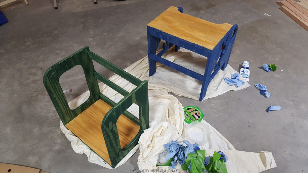 Kid's step stool in two halves still being painted. The bottom half of the step stool is painted yellow and blue and has bunny cutouts. The top part is yellow and green.